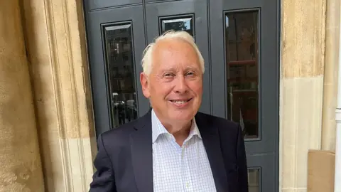 Sir Bob Neill in front of a building with large doors