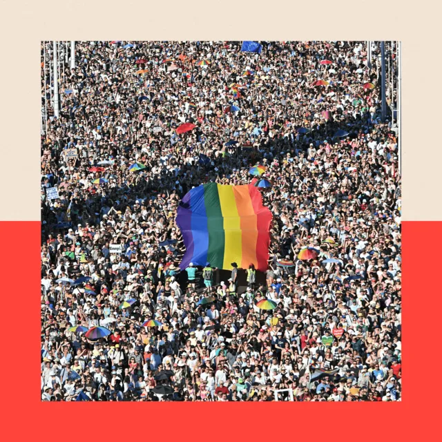 Thousands of people participating in the Budapest Pride march, waving a large LGBT flag.