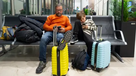 Father and son at airport, looking at flight information