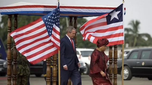 Former US President George W. Bush and former Liberian President Ellen Johnson Sirleaf walk past Liberian and US flags