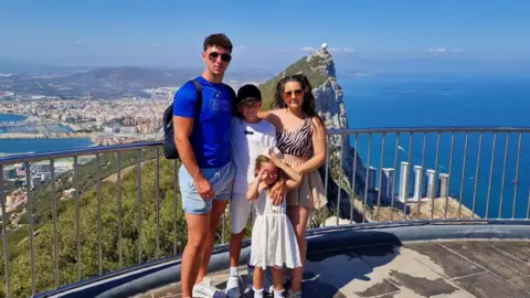 A family posing for a photo with a scenic mountain and coastline view