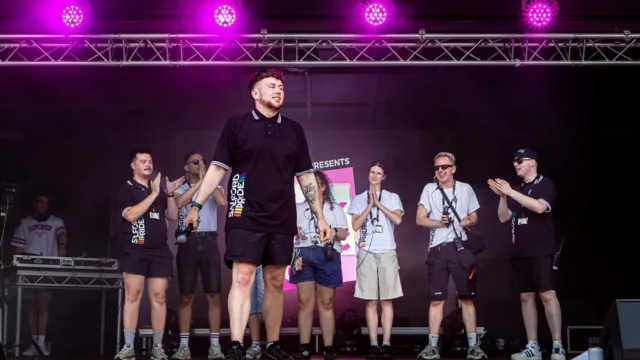 Reece stands on stage at the Pink Picnic event in Salford, holding a microphone.