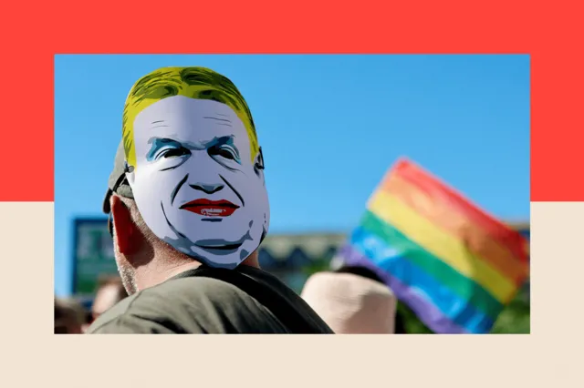A person wearing a mask depicting Viktor Orban's face, with an LGBT flag in the background.