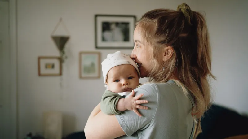 A woman facing left, holding a baby who is looking at the camera.