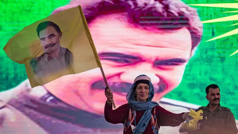 A supporter holding a flag with the face of Abdullah Ocalan, with his face also on the backdrop behind her.
