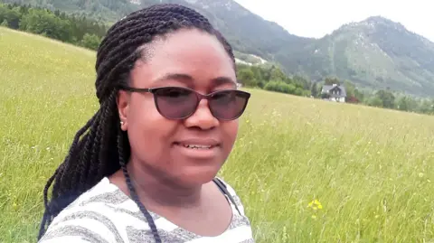 Dr Fortune Gomo wearing sunglasses and braids, posing for a selfie in a meadow.