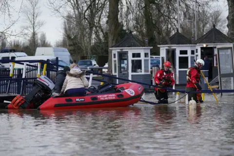 Fire and rescue service personnel wading through floodwaters to rescue people in a boat.