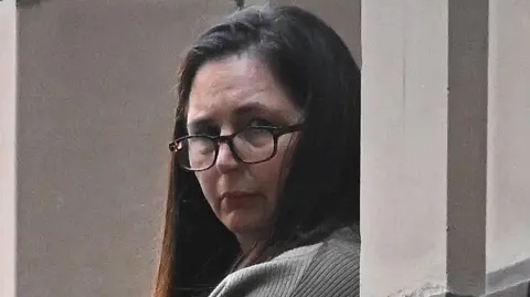 EPA Erin Patterson wearing glasses and a grey knit top looks at the camera