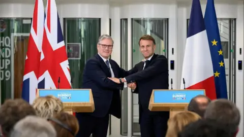 Sir Keir Starmer and French President Emmanuel Macron shaking hands in front of two podiums.
