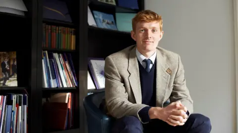 Will Orr-Ewing sat in front of shelves filled with books