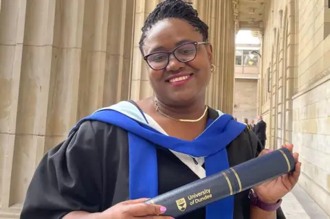 Dr Fortune Gomo in graduation robes, holding a University of Dundee scroll.