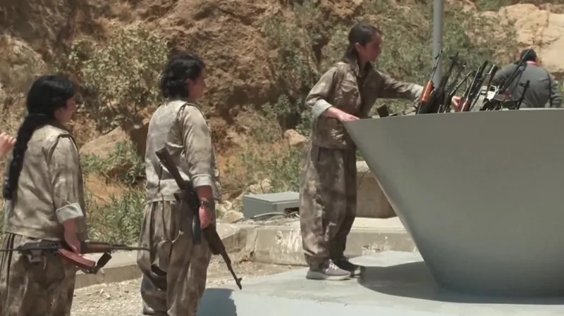 PKK fighters, men and women, placing their guns in a large cauldron to be burned.
