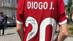 A red Liverpool shirt with the number 20, name \'Diogo J.\' and a small autograph that reads: Um abraço para o Fábio