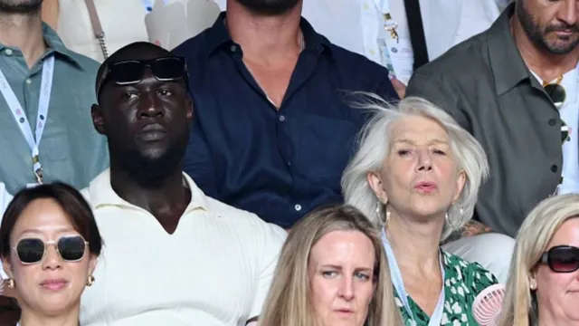 Stormzy, wearing a white polo shirt, sits next to Helen Mirren and Taylor Hackford.