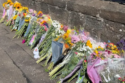 Bunches of flowers with messages left on a pavement near the incident scene.