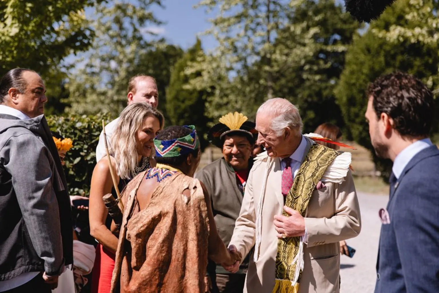 King Charles talks with a man wearing what looks like an animal skin cape at the Harmony Summit.