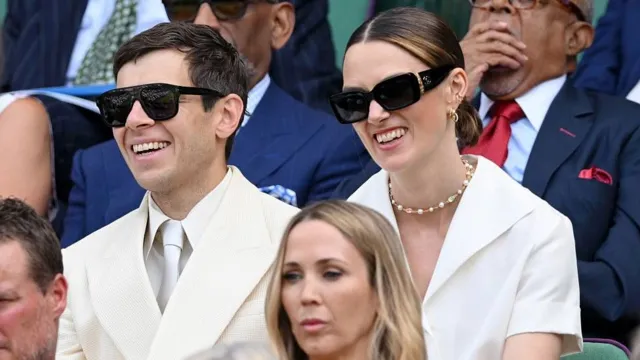 James Righton and Keira Knightley sit side-by-side and smile in the direction of the court.