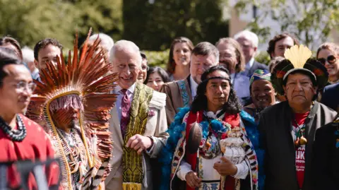 King Charles III and delegates at the Harmony Summit, including individuals in traditional dress and a feathered headdress.