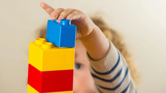A stock image of a young child playing with colourful building blocks.