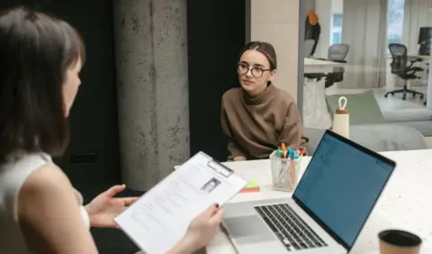 Woman holds CV of a young woman sat in front of her in an office setting