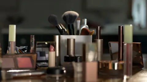 A collection of makeup products, including mascara, eyeshadow, and brushes, are laid out on a surface.